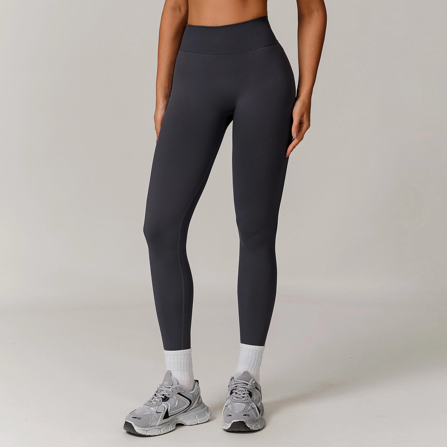 Person wearing black leggings and gray sneakers on a plain background