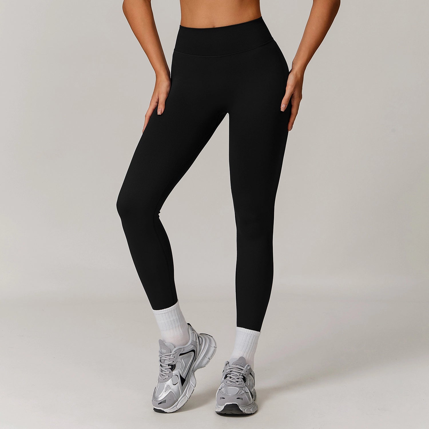 Person wearing black leggings and gray sneakers on a plain background
