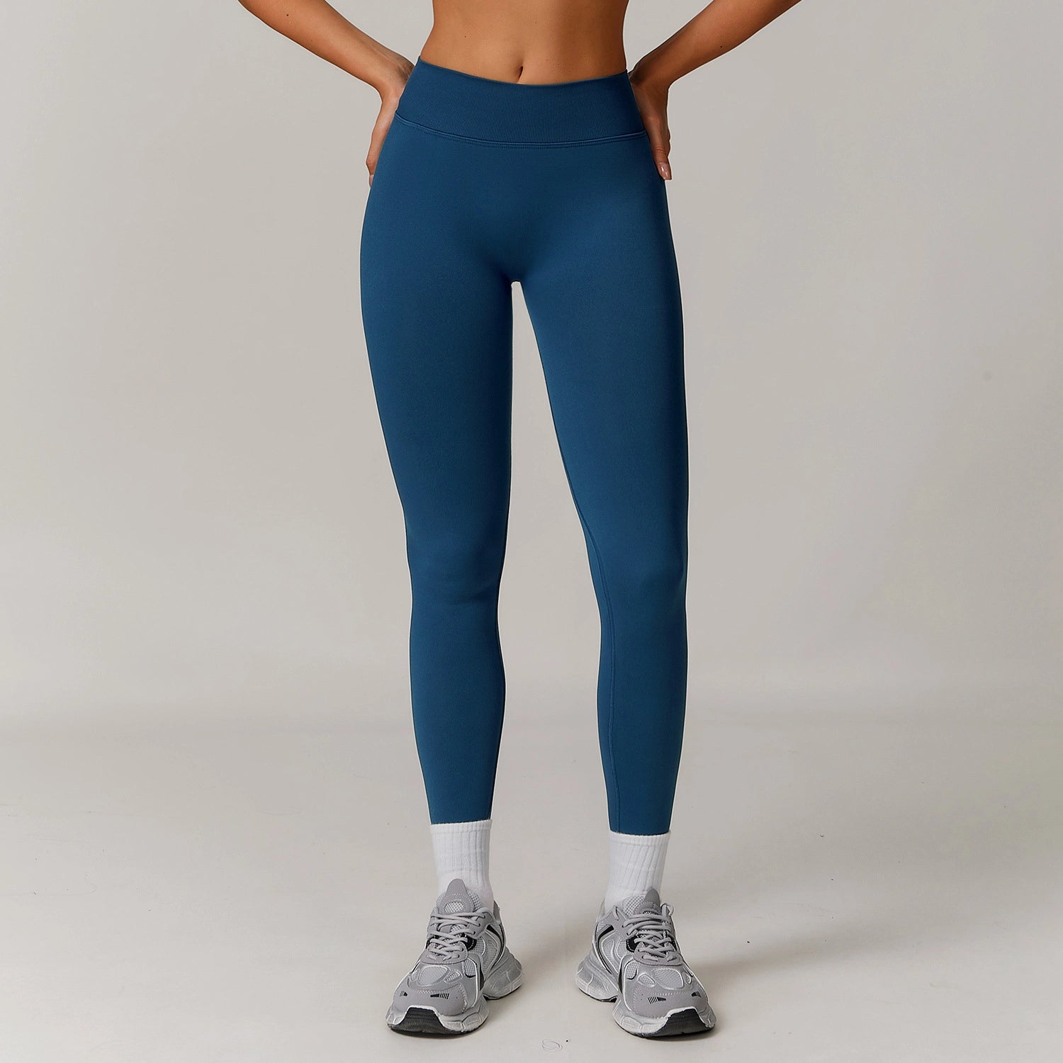 Person wearing blue leggings and gray sneakers on a plain background