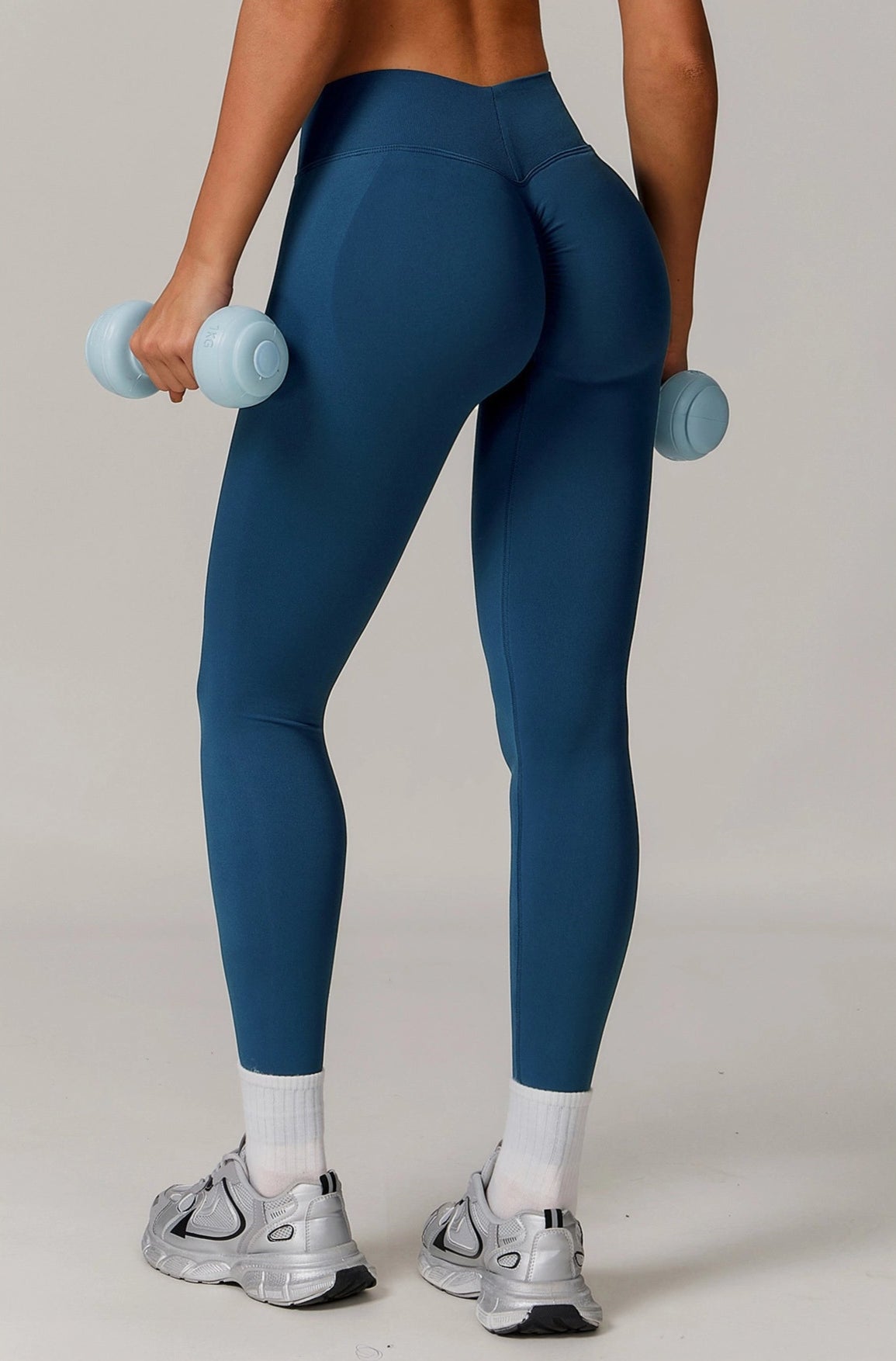 Person wearing blue leggings and white sneakers holding blue dumbbells on a plain background
